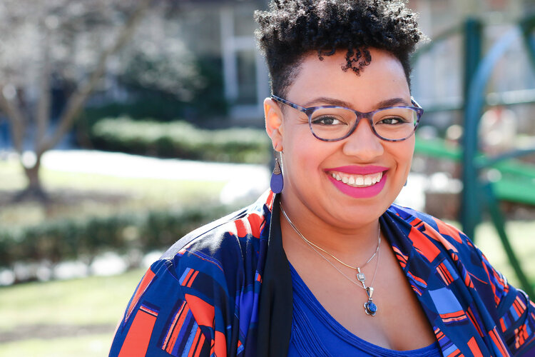 Courtney Harge, CEO. A Black woman with short hair  and wearing glasses and a brightly colored shirt, smiling widely.