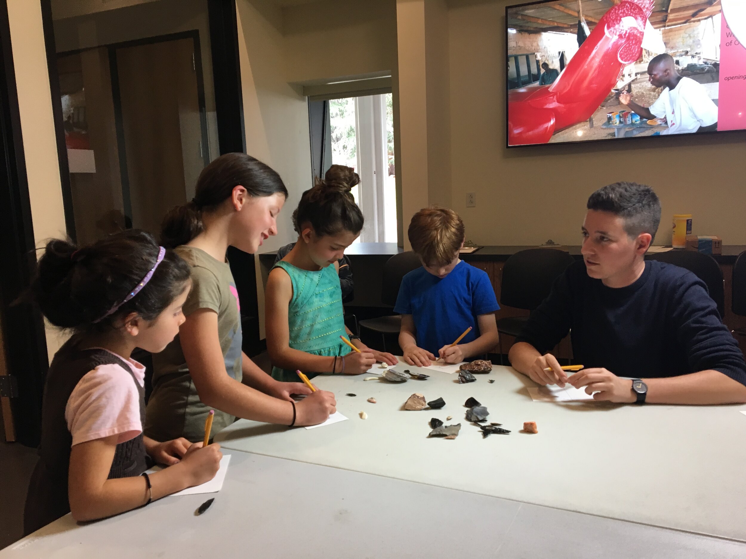 Katie Fleming, Gallery Manager & Education Coordinator at the Phoebe A. Hearst Museum of Anthropology, working with four children on a creative project.