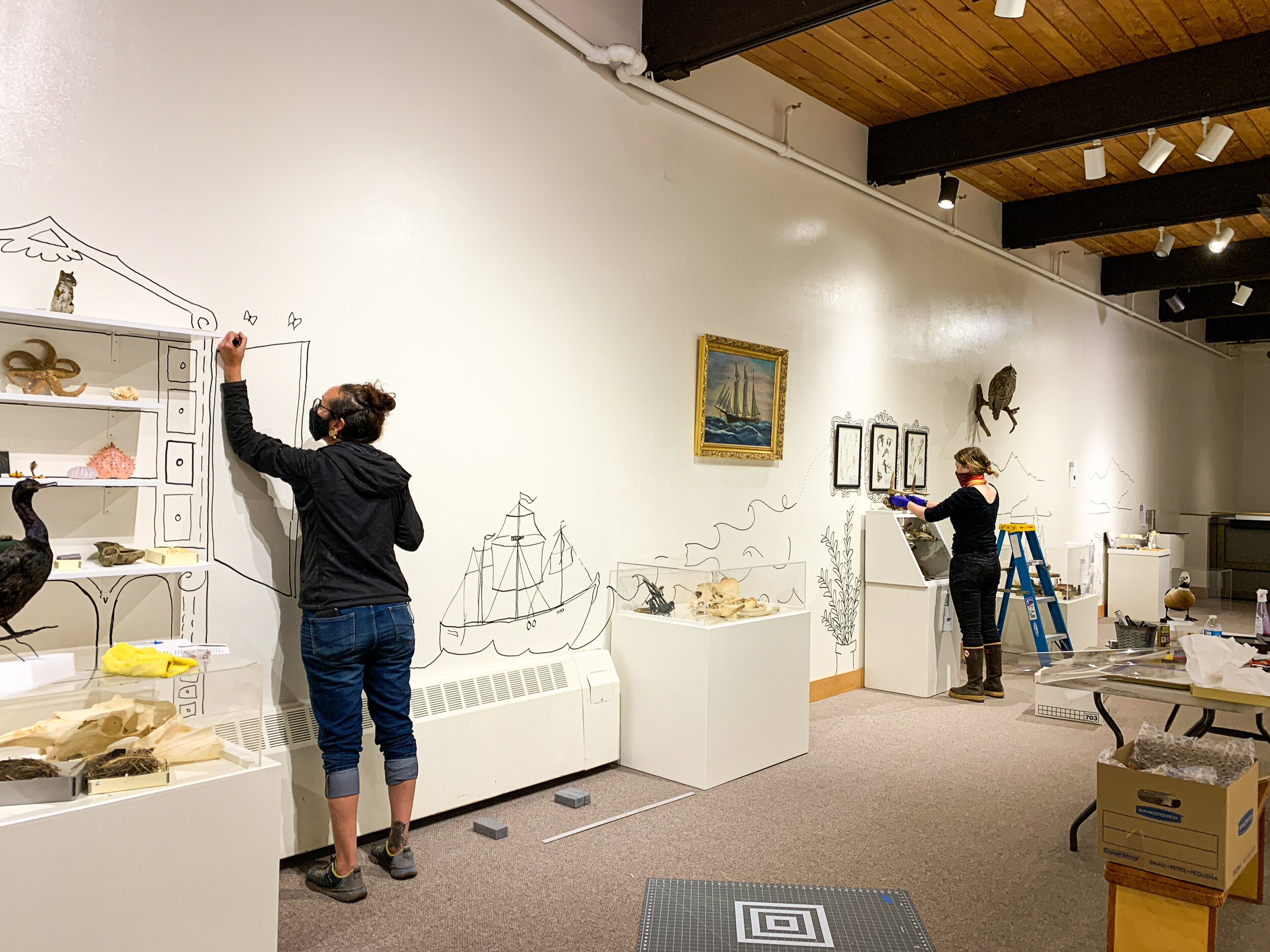Jennifer Gibbins, Executive Director of Pratt Museum in Homer, AK, and museum staff member install a gallery exhibition.